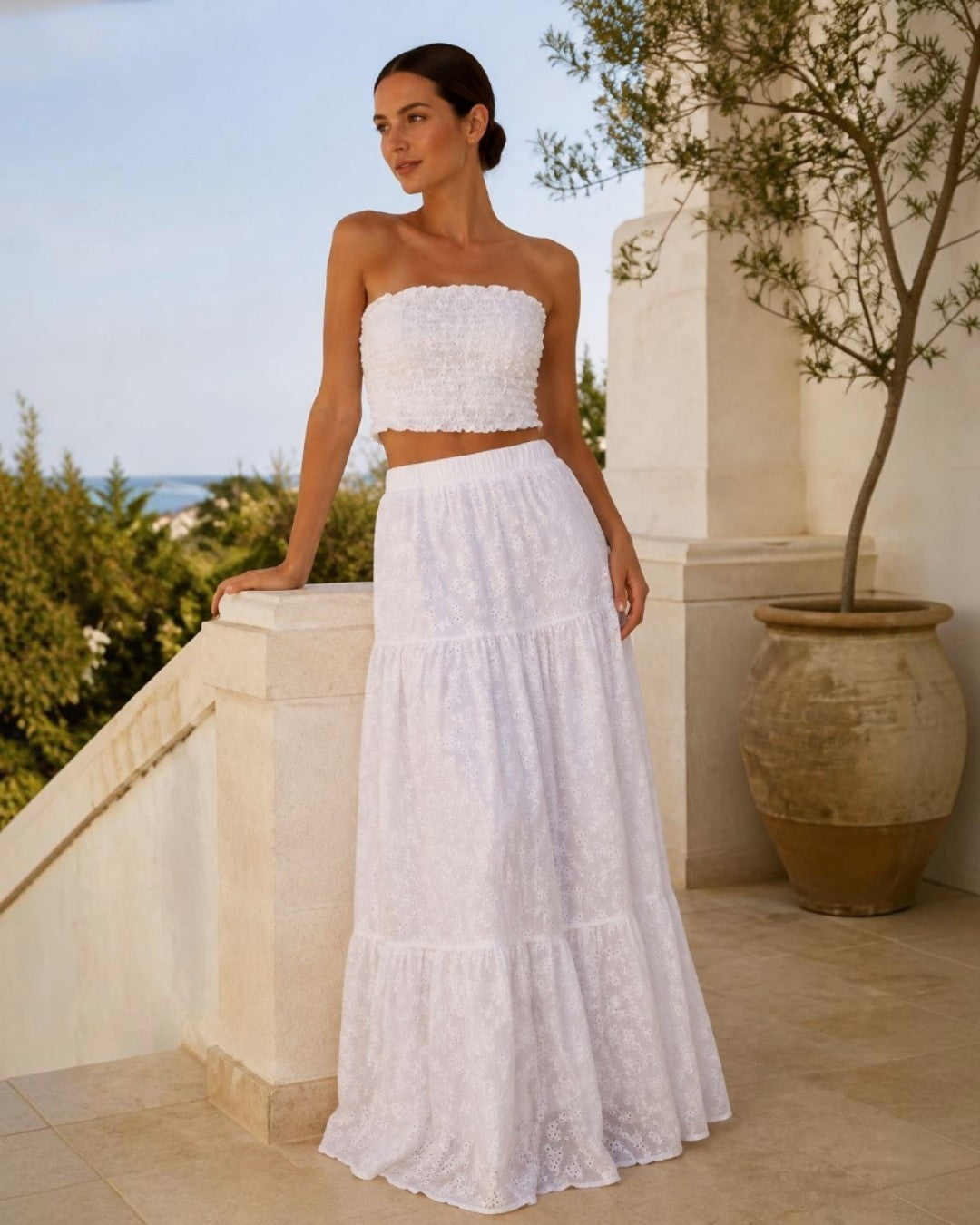 Woman in a white broderie anglaise top and maxi skirt on a sunlit terrace